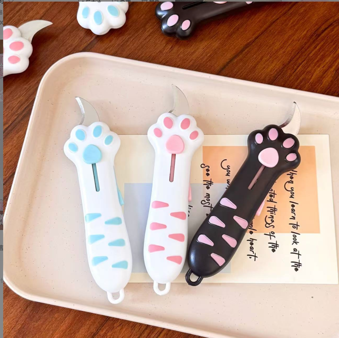 Three cat paw retractable box cutters arranged on a tray in blue, pink and black colorways.
