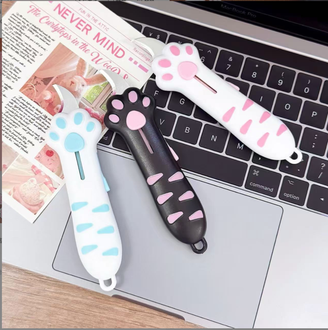 Three cat paw retractable box cutters displayed on a laptop beside a magazine.