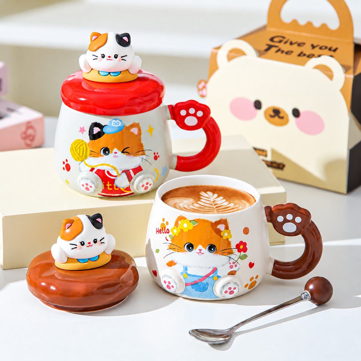 Brown cat mug filled with coffee beside its lid, with a red mug behind.
